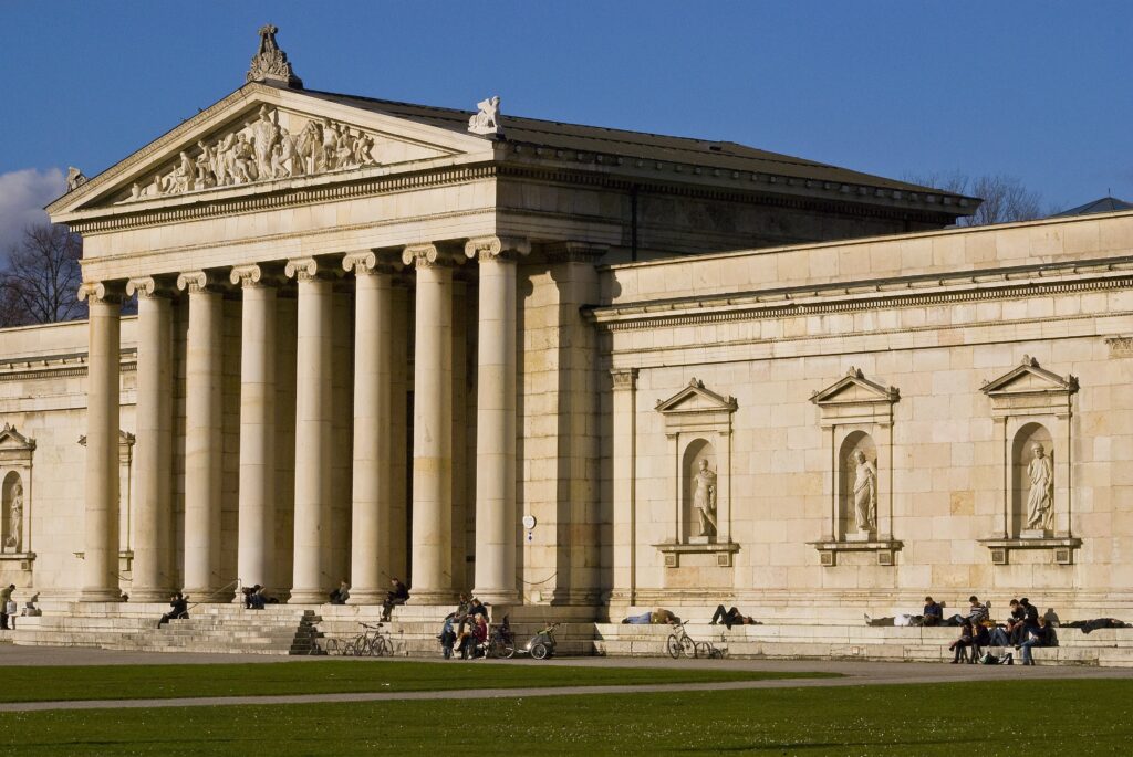 Die Glyptothek wurde im Auftrag des Königs Ludwig I. in den Jahren 1816 bis 1830 von Leo von Klenze zur Ausstellung antiker Plastiken am zentralen Königsplatz der neuen Stadtachse errichtet. Hauptwerke der Sammlung sind vor allem der Barberinische Faun, die sogenannte Trunkene Alte, der Knabe mit der Gans, die Eirene mit dem Ploutosknaben und die 1813 erworbenen wertvollen Giebelfiguren vom Aphaia-Tempel in Ägina, die so genannten Ägineten sowie die beiden Kouroi, der Münchner Kouros und der Kouros von Tenea. The Glyptothoth was built on behalf of the King Ludwig I in the years 1816 to 1830 by Leo of Klenze to the exhibition of antique sculptures at the central royal square of the new city axis. Main works of the collection are mainly the Barberian Faun, the so-called drunken old, the boy with the goose, the Eisen with the Ploutosknoben and the 1813 acquired valuable gable figures from the Aphaia Temple in Aegina, the so-called Aeginen and the two Kouroi, the Munich Kouros and the Kouros of Tenea.